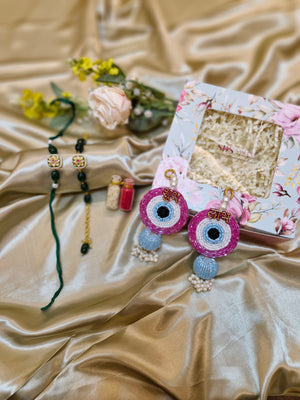 Decorative items including a box with floral design, colorful eye-shaped objects, and a bracelet on a beige fabric background.